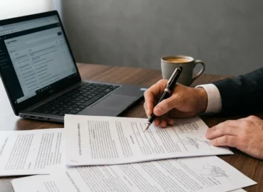 Close-up das mãos de um advogado analisando contrato de imóvel e documentos sobre mesa de madeira com café.