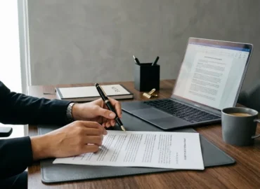 Mãos de um profissional sobre um contrato e documentos jurídicos em uma mesa de escritório elegante com luz natural.