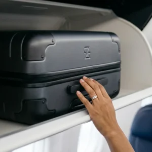 Detalhe de mala de mão em compartimento superior de avião, simbolizando direitos do passageiro.
