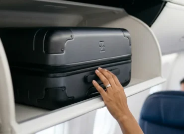 Detalhe de mala de mão em compartimento superior de avião, simbolizando direitos do passageiro.