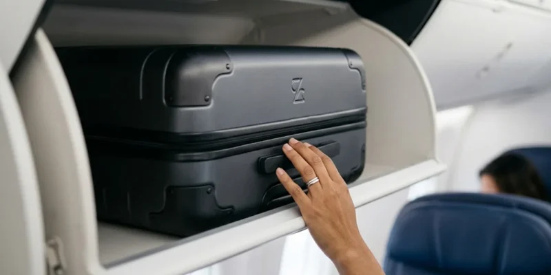 Detalhe de mala de mão em compartimento superior de avião, simbolizando direitos do passageiro.